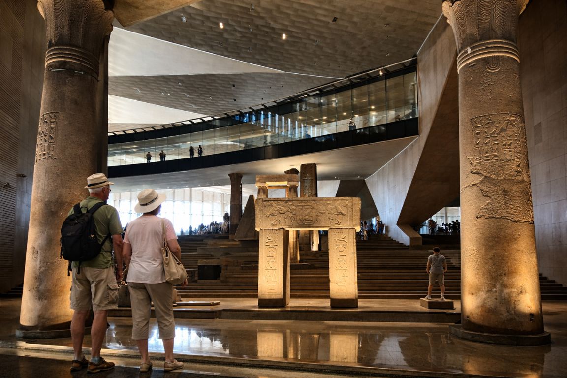 Senior tourists viewing ancient columns and statues inside the Grand Egyptian Museum during a The Grand Egyptian Museum Tickets experience
